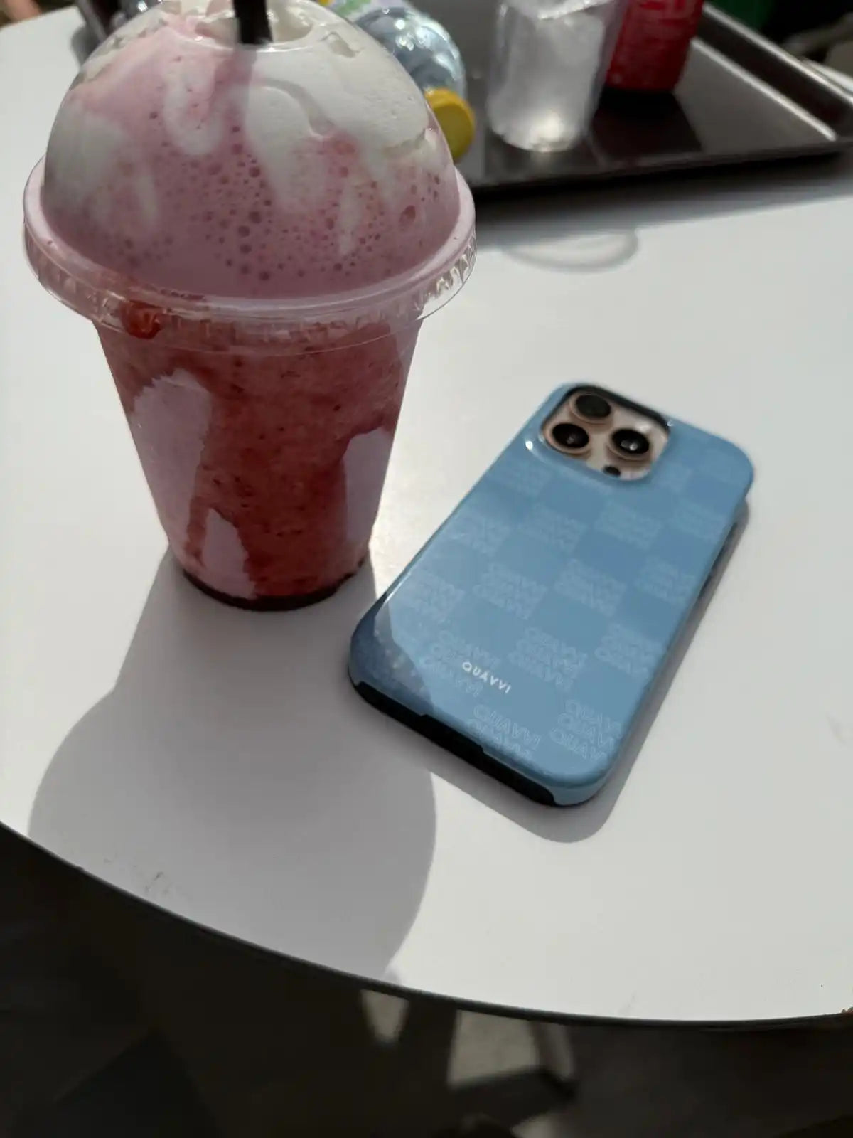 Strawberry smoothie with whipped cream and a blue checkered phone case.